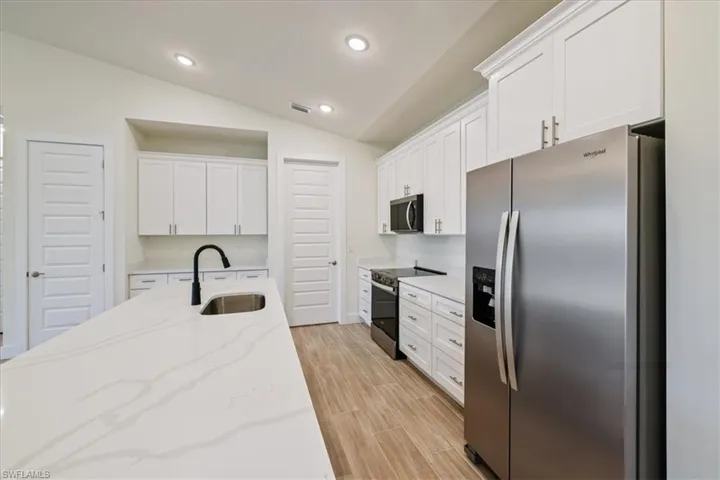 Kitchen featuring stainless steel appliances, vaulted ceiling, white cabinetry, light stone countertops, and recessed lighting