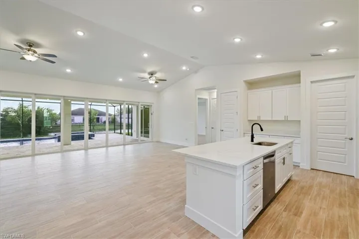 Kitchen with open floor plan, white cabinets, wood finish floors, light stone counters, and recessed lighting