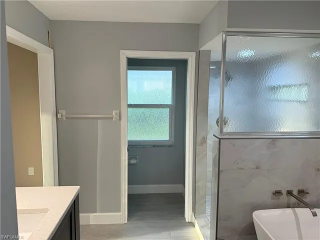 Full bath featuring vanity, a shower stall, a freestanding bath, and light wood finished floors