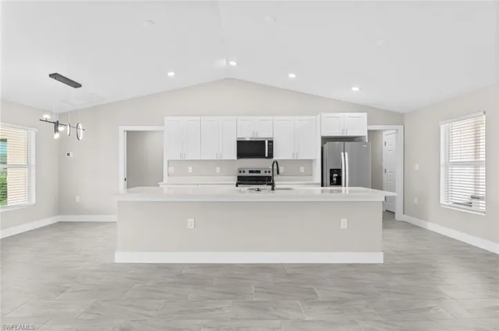 Kitchen with appliances with stainless steel finishes, a kitchen island with sink, lofted ceiling, light countertops, and white cabinets