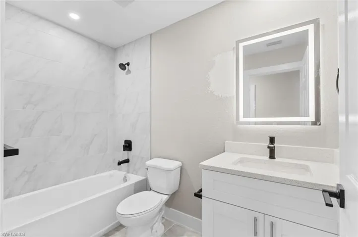 Full bathroom featuring vanity, bathtub / shower combination, a textured wall, and recessed lighting