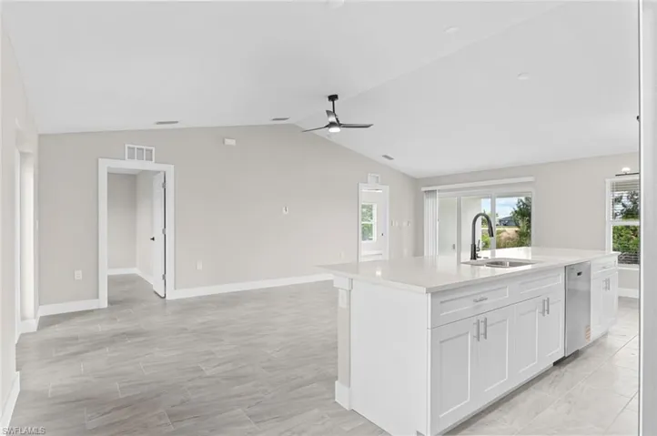 Kitchen featuring open floor plan, vaulted ceiling, an island with sink, white cabinets, and stainless steel dishwasher