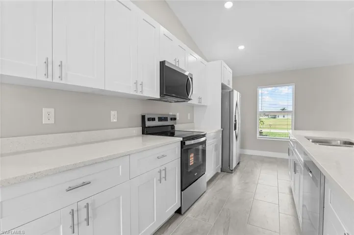 Kitchen featuring appliances with stainless steel finishes, vaulted ceiling, white cabinetry, light stone countertops, and recessed lighting