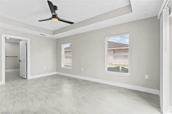 Unfurnished bedroom featuring a raised ceiling, ceiling fan, and a spacious closet