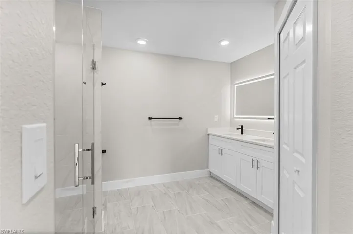Full bath with double vanity, a stall shower, a textured wall, and recessed lighting