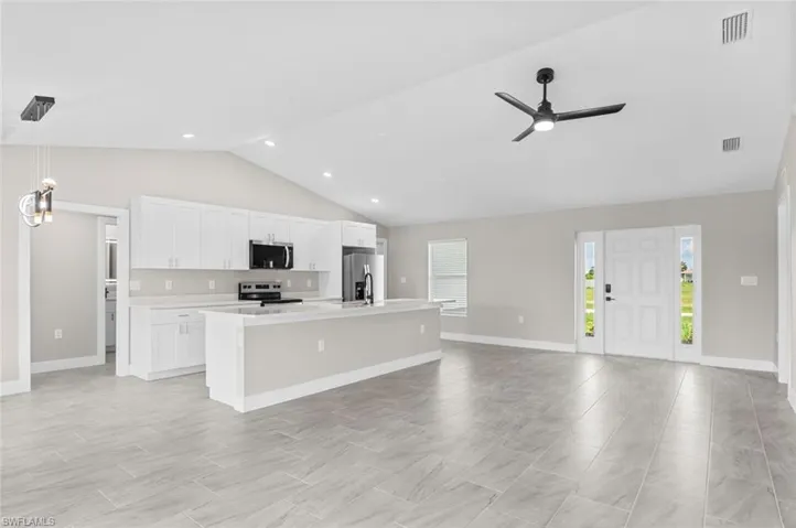 Kitchen with a center island with sink, light countertops, ceiling fan, white cabinets, and open floor plan