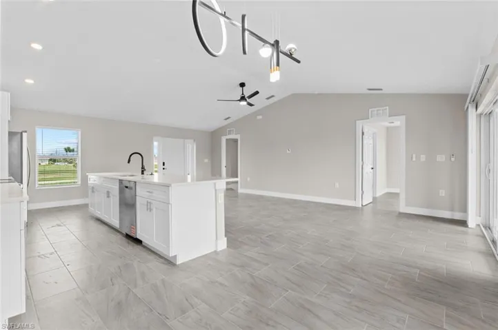 Kitchen with vaulted ceiling, light countertops, ceiling fan, open floor plan, and white cabinetry