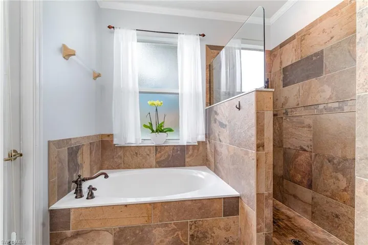 Full bath featuring a walk in shower, ornamental molding, and a garden tub