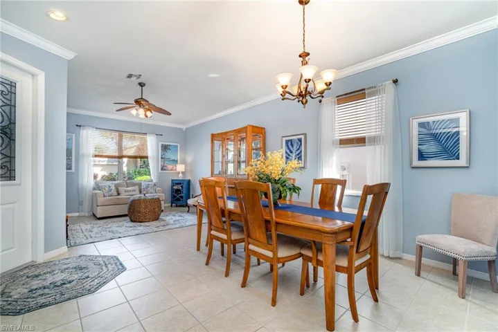 Dining area featuring light tile patterned floors, visible vents, ornamental molding, baseboards, and ceiling fan with notable chandelier