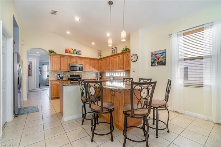 Kitchen featuring pendant lighting, stainless steel appliances, stone countertops, light tile patterned flooring, and a kitchen breakfast bar