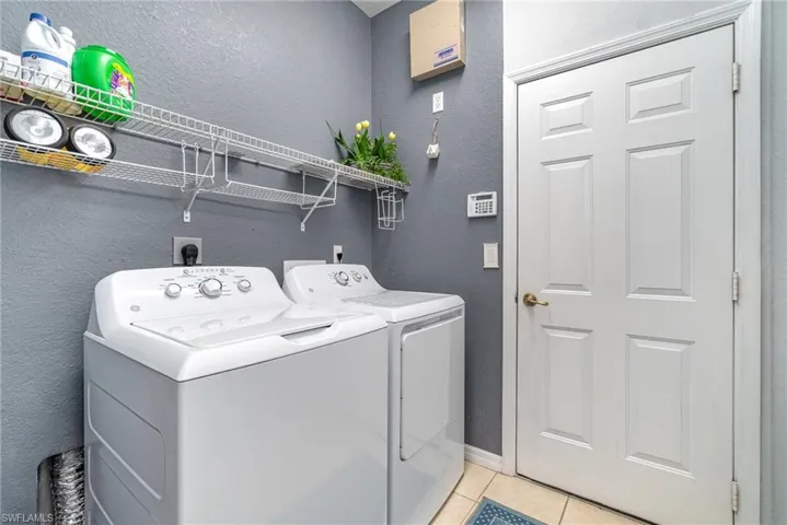 Laundry area featuring light tile patterned floors, a textured wall, laundry area, separate washer and dryer, and baseboards