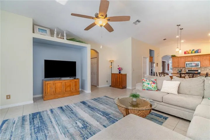 Living room featuring lofted ceiling, light tile patterned floors, arched walkways, and a ceiling fan