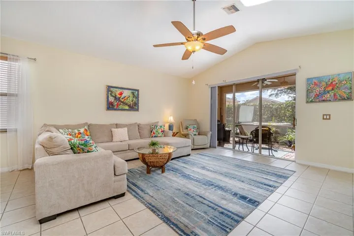 Living area with light tile patterned floors, visible vents, vaulted ceiling, and a wealth of natural light