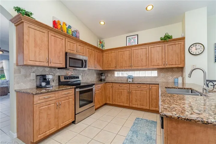 Kitchen with stainless steel appliances, stone counters, light tile patterned flooring, and a sink