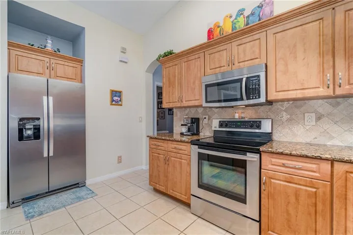 Kitchen with stainless steel appliances, light stone counters, light tile patterned flooring, and tasteful backsplash
