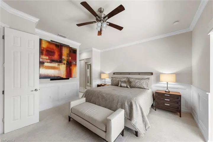 Neutral-toned room featuring crown molding, wainscoting, carpeted flooring, and a ceiling fan with integrated lighting