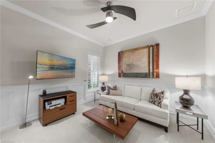 Interior room featuring crown molding, wainscoting, carpeted flooring, window shutters, and a ceiling-mounted fan with integrated lighting