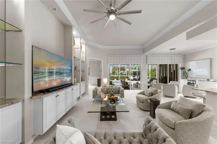Living area featuring high tray ceilings, recessed lighting, built-in cabinetry with stone-finish countertops, glass-shelf accents, and sliding glass doors