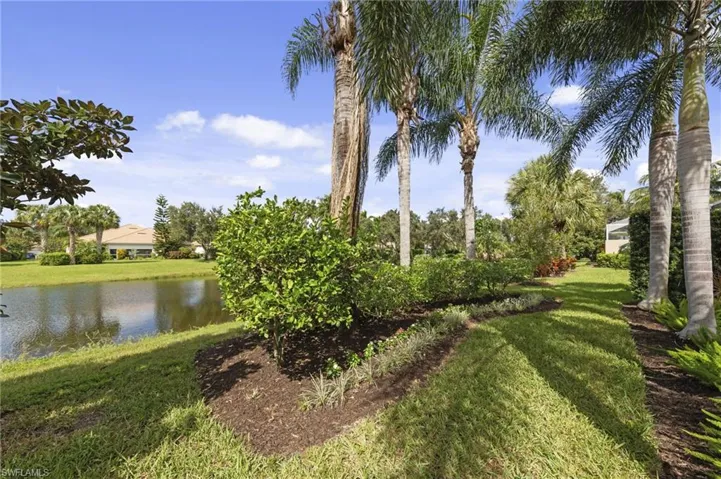 Waterfront backyard featuring mature palm trees, manicured landscaping, and mulch-filled planting beds