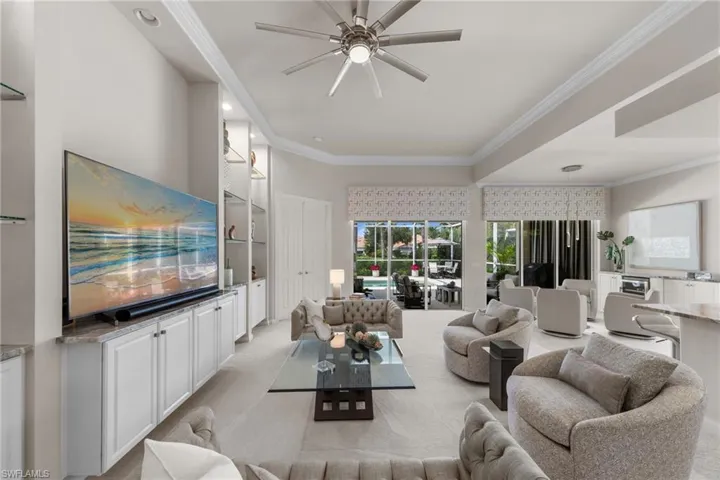 Spacious living area featuring a tray ceiling, recessed lighting, a modern ceiling fan, built-in cabinetry with glass shelving, and sliding glass doors