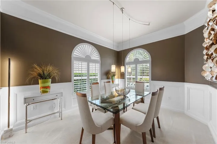 Dining area featuring arched windows with plantation shutters, crown molding, chair rail wainscoting, and modern track lighting