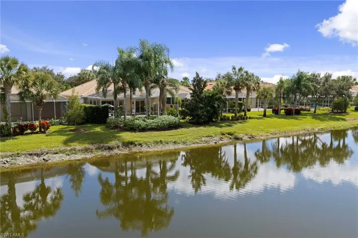 Waterfront property featuring a manicured lawn, mature palm trees, screen-enclosed lanais, and tile roofing