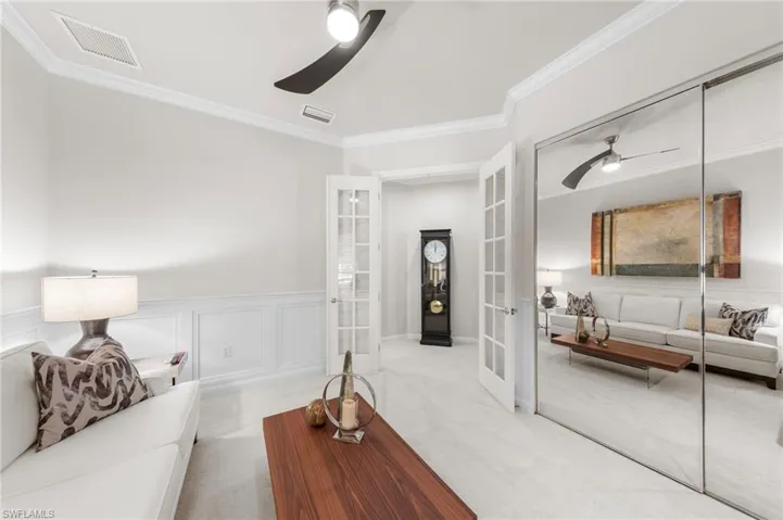 Interior space featuring white wainscoting, polished stone-finish flooring, full-wall mirrored closet doors, dual French glass-paneled doors, and a modern two-blade ceiling fan