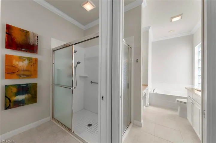 Enclosed glass shower stall with a handheld fixture, built-in soaking tub, tile flooring, crown molding, and glass block window