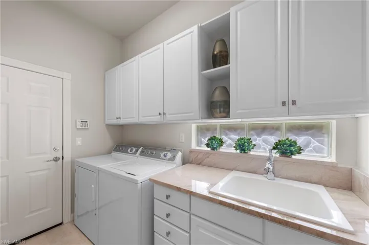 Utility space featuring white cabinetry with brushed metal hardware, a drop-in sink with a gooseneck faucet, light-toned stone-finish countertop, and a textured privacy glass window