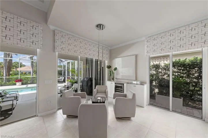 High-ceilinged room featuring ceramic tile flooring, three sets of floor-to-ceiling sliding glass doors, built-in cabinetry with stone-finish countertops, and a glass-door wine refrigerator
