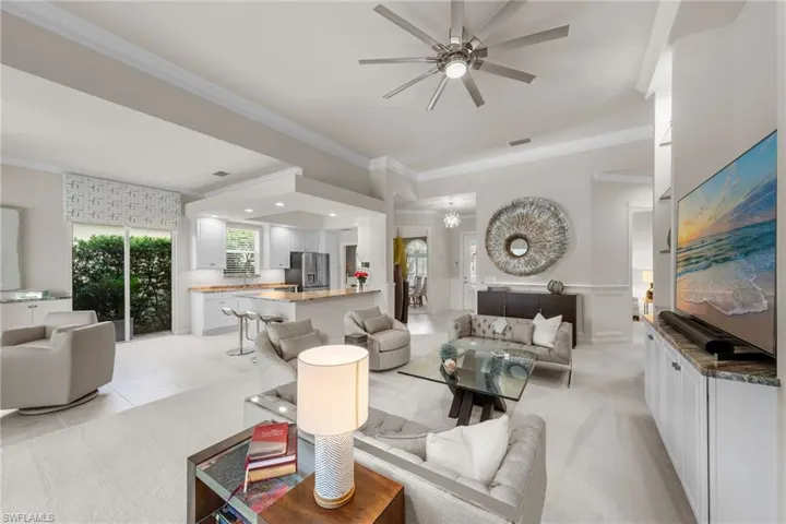 Open-concept interior featuring tray ceilings, neutral wall-to-wall carpeting, custom built-in cabinetry with stone-surface countertops, recessed lighting, and a multi-blade ceiling fan