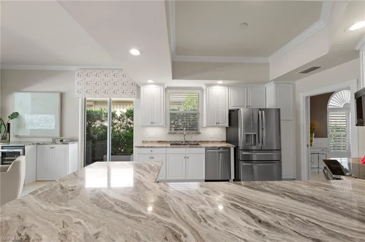 Kitchen featuring white shaker-style cabinetry, natural stone countertops with prominent veining, stainless steel appliances, recessed lighting, and crown molding