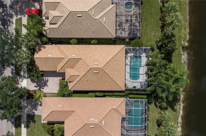 Aerial perspective featuring a shingle-style roof, a screened-in swimming pool enclosure, paver driveway, mature landscaping, and waterfront location