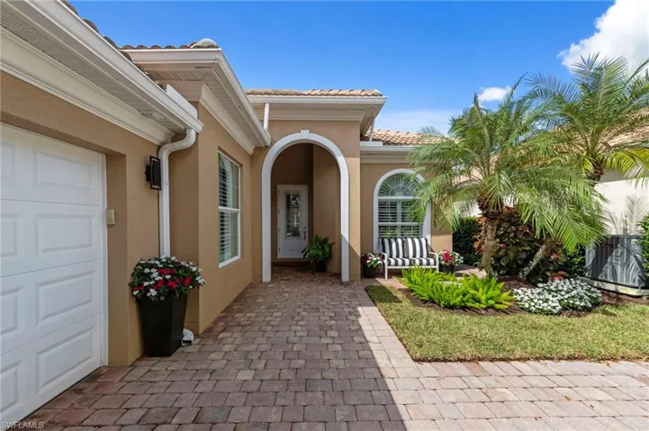 Stucco exterior featuring an arched entryway, paver walkway, arched window with decorative molding, and a paneled garage door