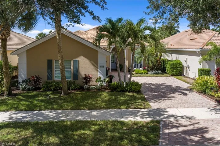 Stucco exterior featuring a paver driveway, arched entryway, and tile roof, surrounded by mature palms and landscaping
