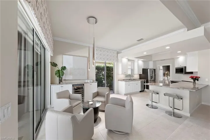 Open-concept kitchen featuring white cabinetry, stone-finish countertops, stainless steel appliances, a built-in wine refrigerator, and tile flooring
