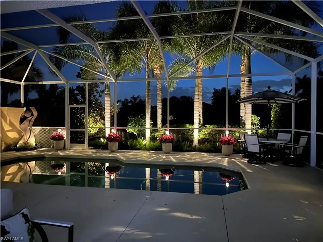 Screen-enclosed pool area featuring concrete decking, perimeter landscape lighting, and mature palm trees
