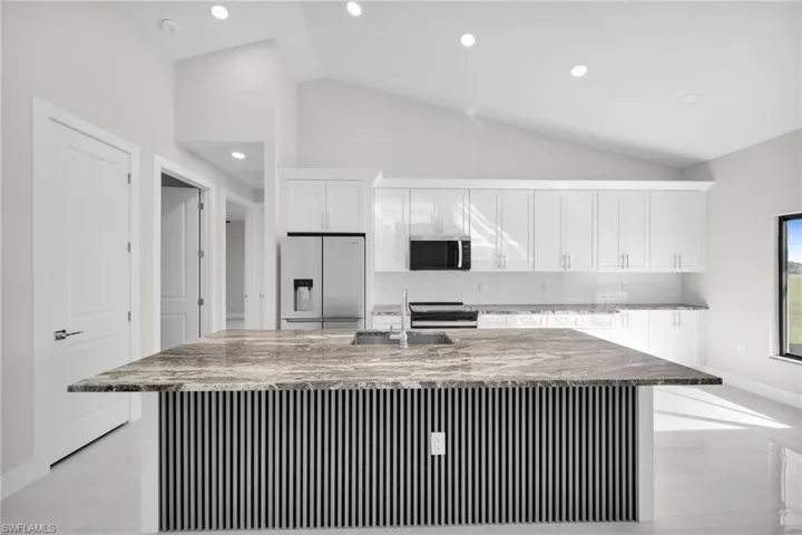 Kitchen featuring white cabinetry, appliances with stainless steel finishes, backsplash, light stone counters, and recessed lighting