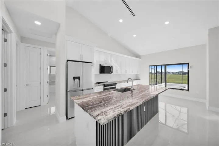 Kitchen with light stone countertops, white cabinetry, stainless steel appliances, recessed lighting, and a center island with sink