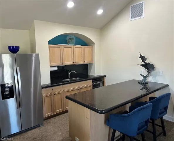 Guest house Kitchen featuring a kitchen breakfast bar, dark colored carpet, backsplash, stainless steel refrigerator with ice dispenser, and sink