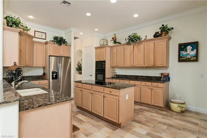 Kitchen with crown molding, a kitchen island, black appliances, dark stone counters, and sink