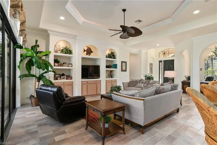 Living room featuring a tray ceiling, crown molding, built in shelves, and ceiling fan