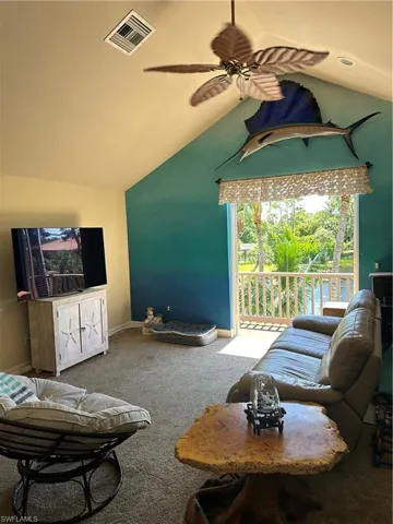 Carpeted guest house living room featuring a wealth of natural light, ceiling fan, and vaulted ceiling access to balcony