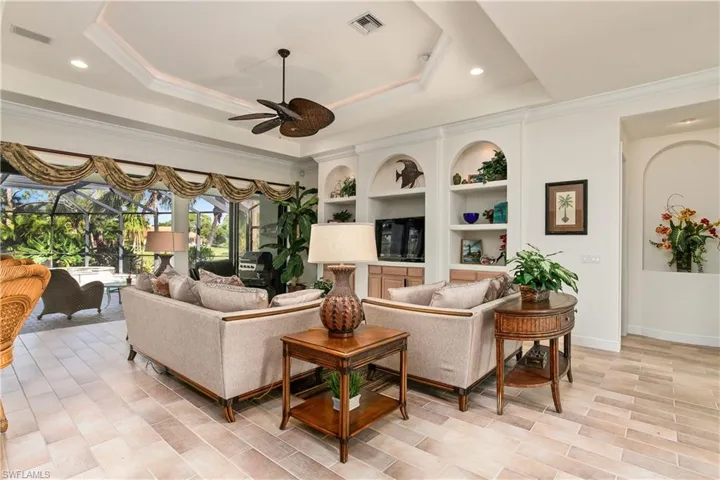 Living room featuring a raised ceiling, ceiling fan, and light tile flooring