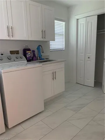Laundry area featuring washer/dryer extra storage and light marble finish flooring