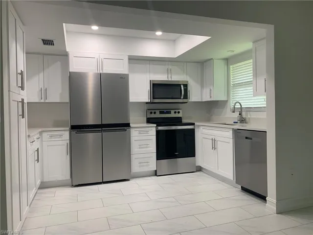 Kitchen with appliances with stainless steel finishes, white cabinetry, light marble finish flooring, recessed lighting, and light stone countertops