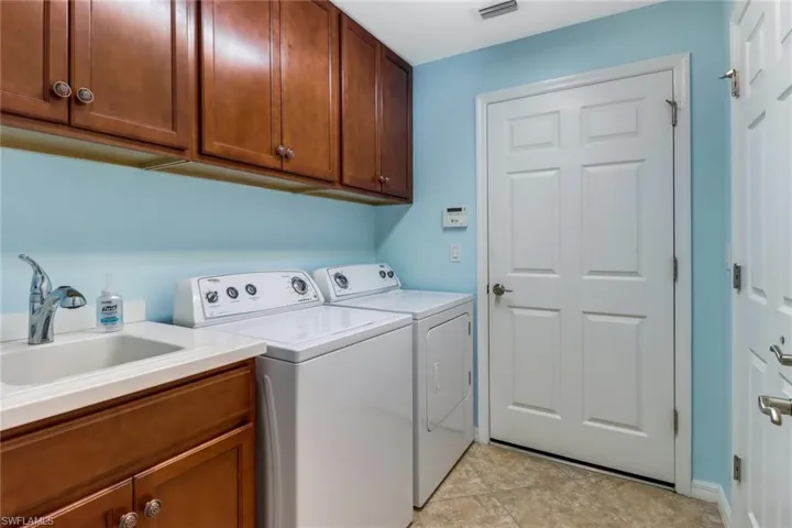 Laundry area with sink, cabinets, washer and dryer, and light tile patterned flooring