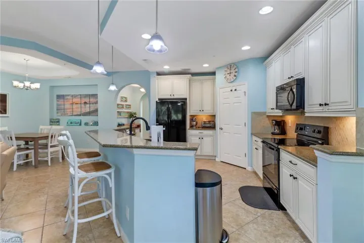 Kitchen with decorative light fixtures, black appliances, a notable chandelier, backsplash, and dark stone counters