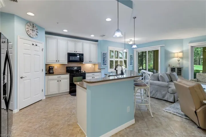 Kitchen with a wealth of natural light, black appliances, hanging light fixtures, and white cabinetry