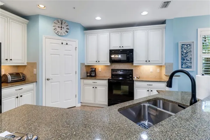 Kitchen with black appliances, sink, white cabinetry, and tasteful backsplash